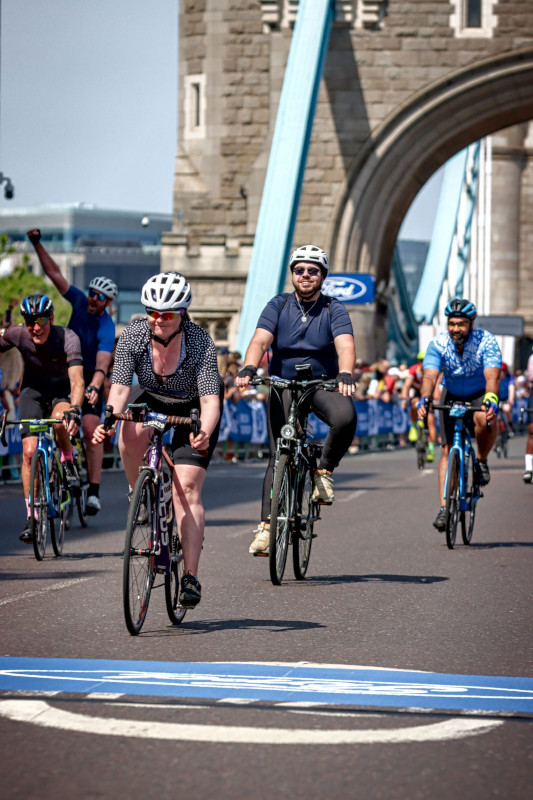 Me on a bike, smiling, with London&rsquo;s Tower Bridge behind me